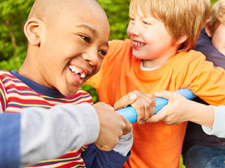 Auf dem Bild sind vier Kinder zu sehen, die auf einem Klettergerüst spielen. Sie lachen. Im Hintergrund ist eine grüne Hecke zu sehen.