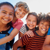 Eine Gruppe von sechs fröhlichen Kindern steht dicht beieinander und lächelt in die Kamera. Sie sind bunt gekleidet. 