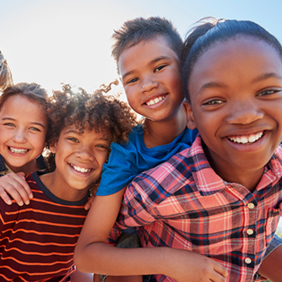Eine Gruppe von sechs fröhlichen Kindern steht dicht beieinander und lächelt in die Kamera. Sie sind bunt gekleidet.