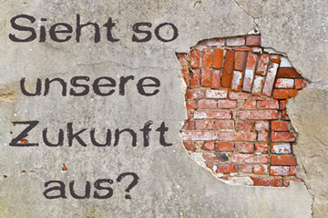 Das Bild zeigt eine Wand mit einer großen, unregelmäßigen Öffnung, durch die rote Ziegelsteine sichtbar sind. Links neben der Öffnung steht in großer, dunkler Schrift die Frage: "Sieht so unsere Zukunft aus?" Die Wand wirkt alt und brüchig, was den Eindruck von Verfall und Zerfall vermittelt.