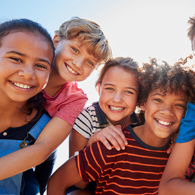 Eine Gruppe von sechs fröhlichen Kindern steht dicht beieinander und lächelt in die Kamera. Sie sind bunt gekleidet.