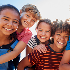 Eine Gruppe von sechs fröhlichen Kindern steht dicht beieinander und lächelt in die Kamera. Sie sind bunt gekleidet.