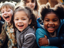 Auf dem Bild sind sechs fröhliche Kinder zu sehen, die eng beieinander stehen und in die Kamera lächeln. Sie befinden sich auf einem Spielplatz im Freien. Die Kinder tragen verschiedene farbenfrohe Kleidung. Im Hintergrund ist eine Holzkonstruktion zu erkennen.