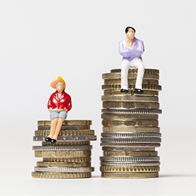 Das Bild zeigt zwei Miniaturfiguren, die auf gestapelten Münzen sitzen. Die linke Figur trägt eine rote Jacke und einen gelben Hut und sitzt auf einem kleineren Stapel Münzen. Die rechte Figur trägt ein lila Oberteil und weiße Hosen und sitzt auf einem höheren Stapel Münzen. Der Hintergrund ist schlicht und weiß.