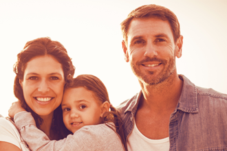 Auf dem Bild ist eine Familie. Links steht die Frau, hat das Mädchen auf dem Arm. Rechts steht ein Mann, der Frau mit Kind zugewandt.
