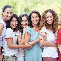 Auf dem Bild stehen sieben Frauen nebeneinander. Alle haben unterschiedlichen Frisuren und unterschiedliche Kleidnug an. Alle lachen und sind fröhlich und gucken nach vorne.