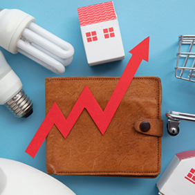 Das Bild zeigt eine braune Geldbörse, auf der ein roter Pfeil in Form eines steigenden Diagramms platziert ist. Um die Geldbörse herum sind verschiedene Gegenstände angeordnet: zwei Glühbirnen, ein Miniatur-Einkaufswagen und zwei kleine Häuser. Der Hintergrund ist hellblau. Das Bild symbolisiert steigende Kosten oder Preise in verschiedenen Lebensbereichen wie Energie, Wohnen und Konsumgüter.