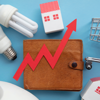 Das Bild zeigt eine braune Geldbörse, auf der ein roter Pfeil in Form eines steigenden Diagramms platziert ist. Um die Geldbörse herum sind verschiedene Gegenstände angeordnet: zwei Glühbirnen, ein Miniatur-Einkaufswagen und zwei kleine Häuser. Der Hintergrund ist hellblau. Das Bild symbolisiert steigende Kosten oder Preise in verschiedenen Lebensbereichen wie Energie, Wohnen und Konsumgüter.
