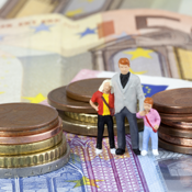Das Bild zeigt drei Miniaturfiguren, die eine Familie darstellen, bestehend aus einem Erwachsenen und zwei Kindern. Sie stehen auf einem Haufen von Euro-Münzen und -Scheinen. Die Münzen sind in verschiedenen Größen gestapelt, und die Scheine sind im Hintergrund sichtbar.