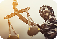 Das Bild zeigt eine Nahaufnahme einer Statue der Justitia, der römischen Göttin der Gerechtigkeit. Die Figur ist mit verbundenen Augen dargestellt, was für Unparteilichkeit steht. In ihrer rechten Hand hält sie eine Waage. Die Statue ist in einem bronzenen Farbton gehalten.