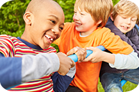 Auf dem Bild sind vier Kinder zu sehen, die auf einem Klettergerüst spielen. Sie lachen. Im Hintergrund ist eine grüne Hecke zu sehen.